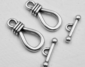 May include: Two silver-toned toggle clasps with a loop on one end and a bar with two round balls on the other end. Two silver-toned loop clasps with a knotted design.