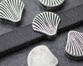 May include: Silver-toned metal seashell charms with a textured, ribbed design. The charms are on a black leather strap.