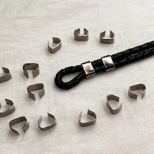 May include: A close-up of a black leather cord with silver metal clasps. There are 12 silver metal cord end caps arranged in a circle around the cord.