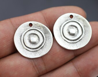 Peut inclure: Deux breloques en métal argenté de forme circulaire. Chaque breloque présente un cercle surélevé au centre avec un cercle plus petit à l'intérieur. Les breloques ont un trou en haut pour être attachées à des bijoux ou d'autres objets artisanaux.