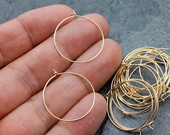 May include: A close-up of a pile of gold-colored hoop earrings. The earrings are made of thin wire and have a simple, classic design.