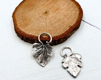 May include: Two silver leaf charms with a loop at the top. The leaves are detailed and have a textured finish.