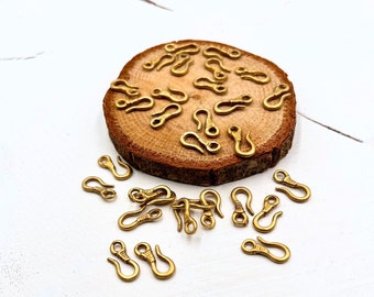 May include: A group of gold-toned metal lobster clasps on a wooden surface. The clasps are small and have a simple design.