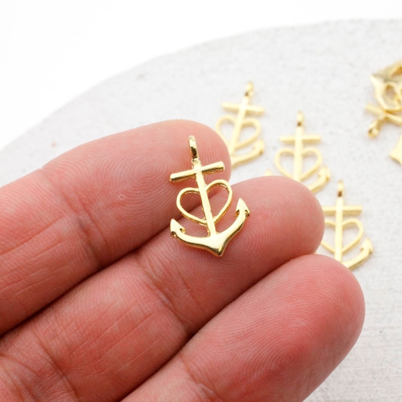 May include: Gold-toned metal charm featuring an anchor with a heart in the center. The anchor has a cross at the top.