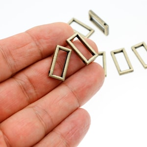 May include: A close-up of a hand holding several antique gold-toned metal rectangular rings. The rings have a smooth, polished finish and are ideal for adding a vintage touch to crafts and jewelry.