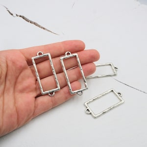 May include: Four silver-toned metal rectangular frames with a hammered texture. Each frame has two jump rings at the top for attaching to jewelry or other crafts.