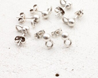May include: A collection of silver-colored earring components, including ball studs with attached loops and butterfly-style earring backs. The components are scattered on a textured, off-white surface.
