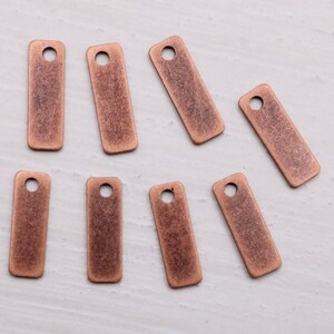 May include: Eight antique copper-toned metal tags with a hole at the top. The tags are rectangular and have a slightly textured surface.