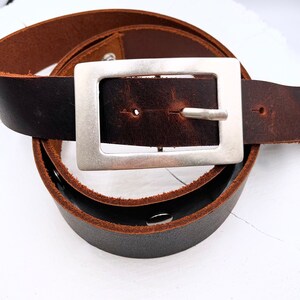 May include: A brown leather belt with a silver buckle. The belt is folded in half and the buckle is in the center of the image.