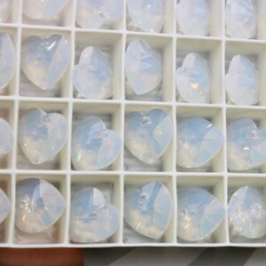 May include: A white plastic container filled with clear, iridescent heart-shaped crystal beads. The beads are arranged in rows and columns.