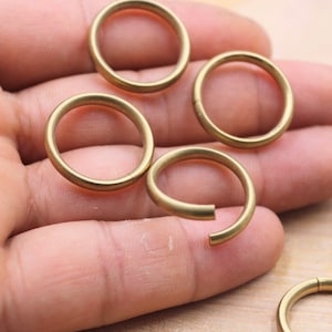 Könnte beinhalten: Vier goldfarbene Metallringe, wahrscheinlich Schlüsselringe, werden auf einer Hand gezeigt. Die Ringe sind alle gleich groß und gleich geformt und aus einem glatten, glänzenden Metall gefertigt.