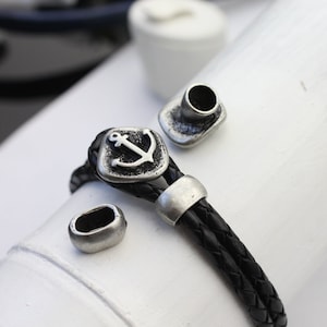 May include: A black leather bracelet with a silver anchor charm and two silver end caps.