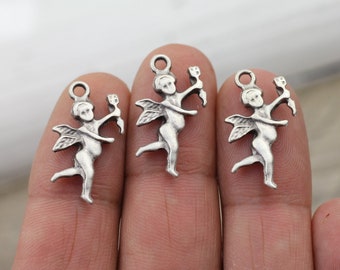 May include: Three silver-toned cherub charms with wings and holding a flower. The charms are on a finger.