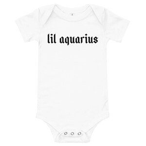 May include: White baby onesie with short sleeves and black text that reads "lil aquarius" in a gothic font.