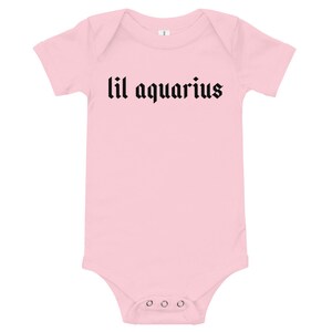 May include: Pink baby onesie with black text that reads "lil aquarius".