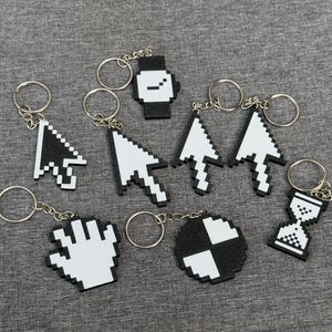 May include: A collection of black and white pixelated keychains. Designs include a watch, arrows, a hand, a circle, and an hourglass. Each keychain has a silver ring attached.