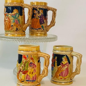 May include: Four vintage ceramic beer steins with detailed relief scenes of people in period clothing. The steins have a tan base, dark blue background, and ornate handles. The scenes depict musicians and dancers.