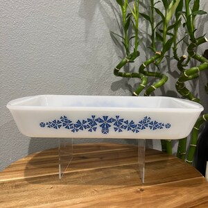 May include: White rectangular baking dish with a blue floral design. The dish is on a wooden surface and is supported by clear acrylic stands.
