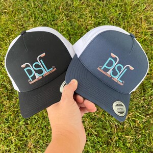 Puede incluir: Dos gorras de camionero, una negra y otra azul marino, con paneles de malla blanca. Ambas gorras presentan un logotipo blanco con el texto "PSL Paramount Streetlight" y un gr&aacute;fico de tres farolas.