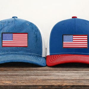 May include: Two baseball caps with the American flag patch. One cap is blue with a white mesh back, and the other is blue and red with a white mesh back. Both have a red, white, and blue American flag patch.