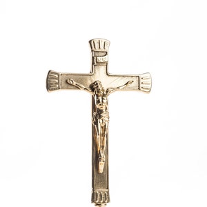 Puede incluir: Un crucifijo de metal dorado con una figura de Jesucristo en la cruz. El crucifijo está montado en un soporte decorativo con una base redonda.