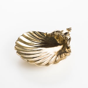 Può includere: Un piatto decorativo a forma di conchiglia dorata con un design ornato dettagliato sul manico.