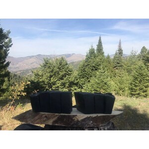 Peut inclure: Deux barres de savon rectangulaires noires sur une surface en bois avec une vue sur une for&ecirc;t et des montagnes en arri&egrave;re-plan.