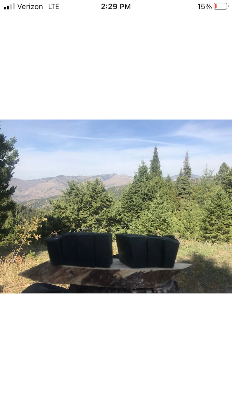 Peut inclure: Deux barres de savon rectangulaires noires sur une surface en bois avec une vue sur une for&ecirc;t et des montagnes en arri&egrave;re-plan.