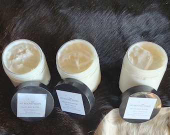 Peut inclure: Trois pots de beurre corporel blanc avec des couvercles et des étiquettes noirs. Les étiquettes indiquent "MT Bound Soaps Tallow Body Butter" avec différents parfums : Vanille Menthe poivrée, Noix de coco noire et Noix de coco olive.
