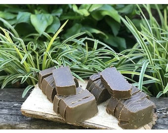 Peut inclure: Gros plan sur plusieurs barres de savon brunes disposées sur un morceau de bois. Le savon est entouré de feuillage vert.