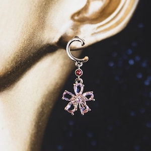 May include: A pair of gold earrings featuring a pink flower design with a red gemstone accent.