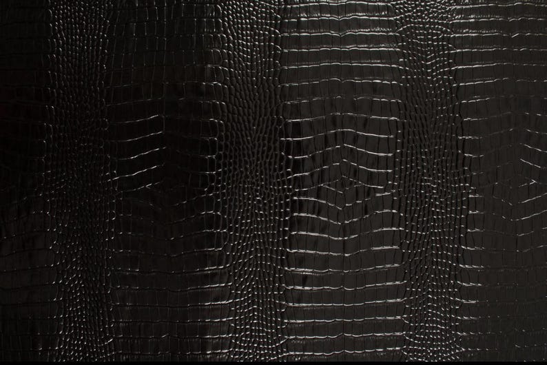 May include: Black crocodile embossed leather texture. The surface has a subtle sheen and a repeating pattern of scales.