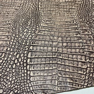 May include: Close-up of a textured surface with a crocodile skin pattern. The pattern features a mix of light beige and dark gray scales, creating a realistic and detailed appearance. The design is suitable for various crafting projects.