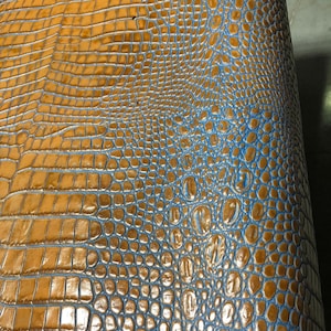 May include: Close-up of a brown and blue crocodile skin leather. The leather has a textured pattern and a glossy finish.