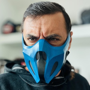 May include: A blue and black face mask with a geometric design. The mask has a mesh section over the mouth and nose. The mask is worn by a person.