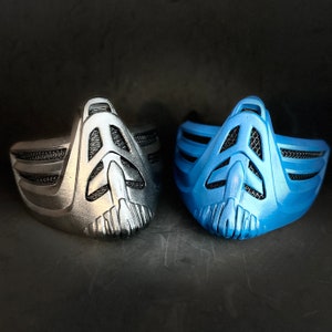 May include: Two face masks, one silver and one blue, with a geometric design. The masks have a raised, textured surface and are made of a durable material.