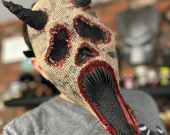 May include: A burlap mask with a skull design, red stitching, and black horns. The mouth is open and has a black and red jagged edge.