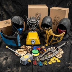 May include: A selection of Mortal Kombat themed items, featuring character masks, a hammer, and keyrings. The masks are in black, blue, red, and gold. A yellow box with "FATALITY" and "MORTAL KOMBAT" is visible. Various other accessories are also included.
