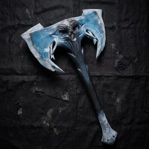 Könnte beinhalten: Fantasy-Axt mit einem Totenkopf-Motiv auf der Klinge. Der Axtkopf ist hellblau mit weißen Akzenten, der Griff dunkelblau. Das Design erinnert an eine Fantasy- oder Mittelalter-Ästhetik.