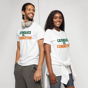 Puede incluir: Dos personas con camisetas blancas con el texto "Catholics vs. Committee" en verde y naranja. El hombre lleva un pantalón de chándal gris y auriculares. La mujer lleva pantalones cortos grises y un suéter blanco atado a la cintura.