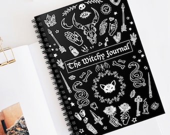 May include: Black spiral bound journal with white illustrations of various witchy symbols, including a cat, snakes, stars, crystals, and the text "The Witchy Journal".