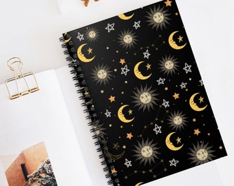 May include: A black spiral notebook with a repeating pattern of gold suns, moons, and stars on a black background.