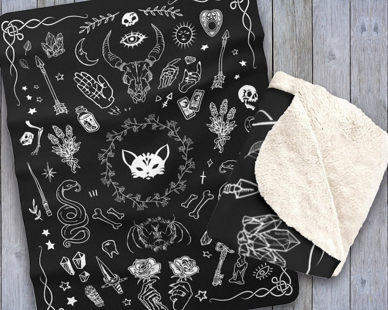Op de afbeelding: Zwart-witte deken met een herhalend patroon van verschillende occulte en mystieke symbolen, waaronder een kat, een schedel, een halve maan, een pentagram, een hand, een slang, een sleutel, een kristal, een bloem en een tarotkaart.