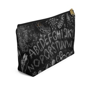 May include: Black zippered makeup bag with a white ouija board design. The design includes the letters of the alphabet, numbers, and symbols.