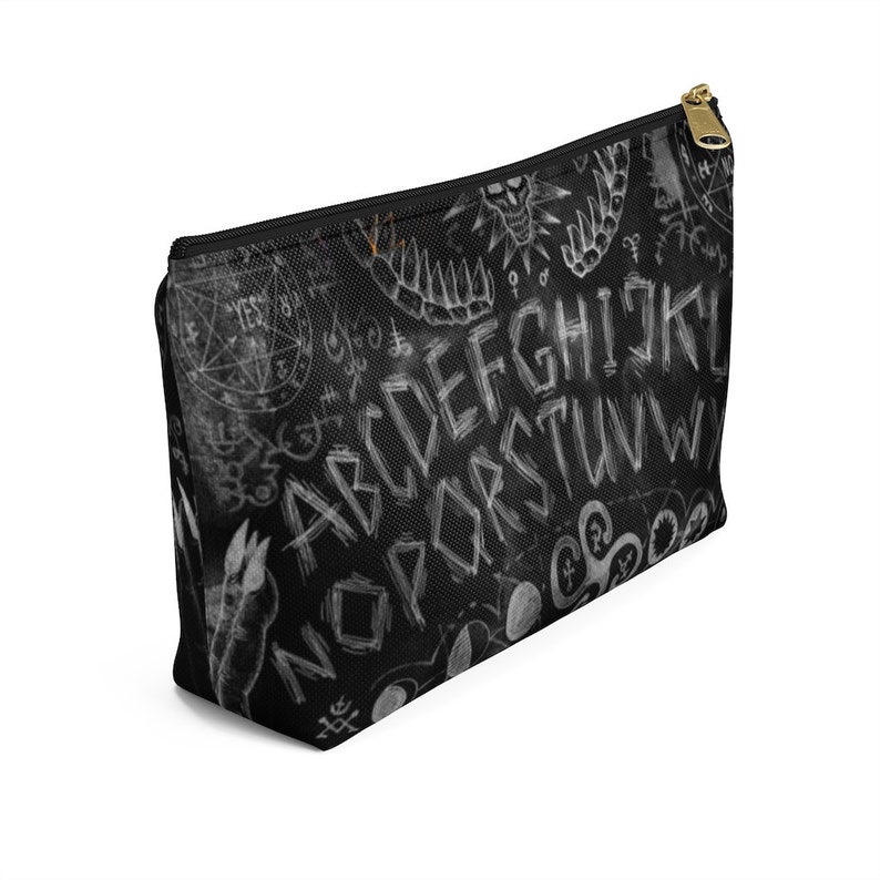 May include: Black zippered makeup bag with a white ouija board design. The design includes the letters of the alphabet, numbers, and symbols.