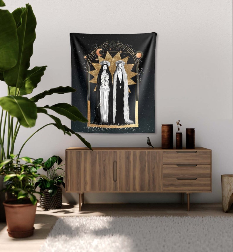 May include: Black tapestry with gold accents featuring two figures in white robes with long black hair. The figures are standing in front of a large gold star with a crescent moon and a sun above them. The background is a dark blue with gold glitter.