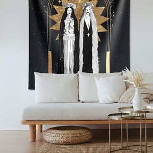 May include: A black tapestry with a gold design of two women standing in front of a large star. The women are wearing white and black robes and have flowers in their hair. The background is a dark blue with stars.