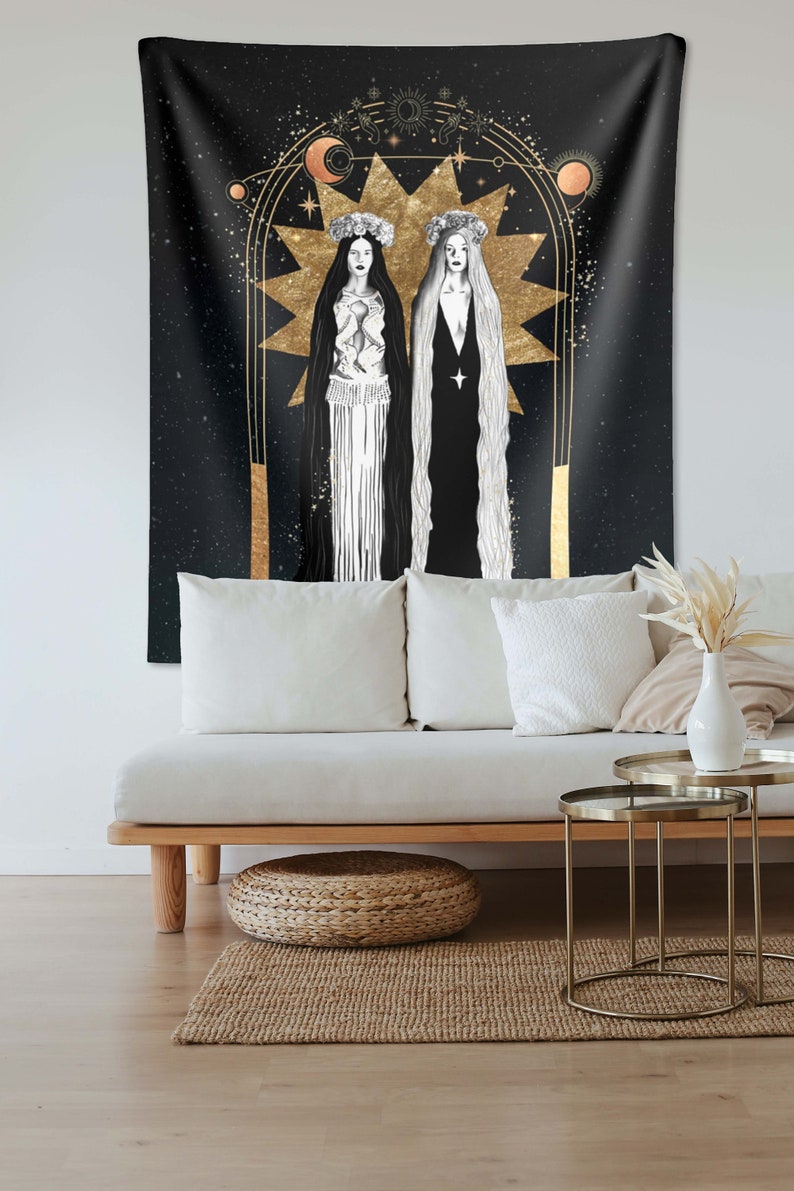 May include: A black tapestry with a gold design of two women standing in front of a large star. The women are wearing white and black robes and have flowers in their hair. The background is a dark blue with stars.