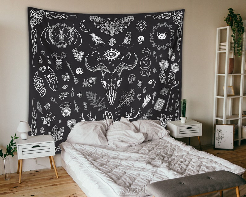 May include: Black and white tapestry with a variety of occult and mystical symbols, including a skull, a snake, a cat, a butterfly, and a hand. The tapestry is hanging on a wall above a white bed with white bedding.
