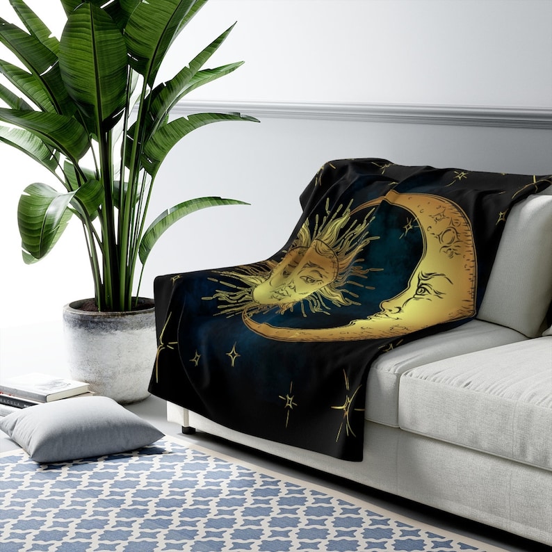 May include: A black fleece throw blanket featuring a gold crescent moon and sun design. The moon and sun have faces and are surrounded by stars.